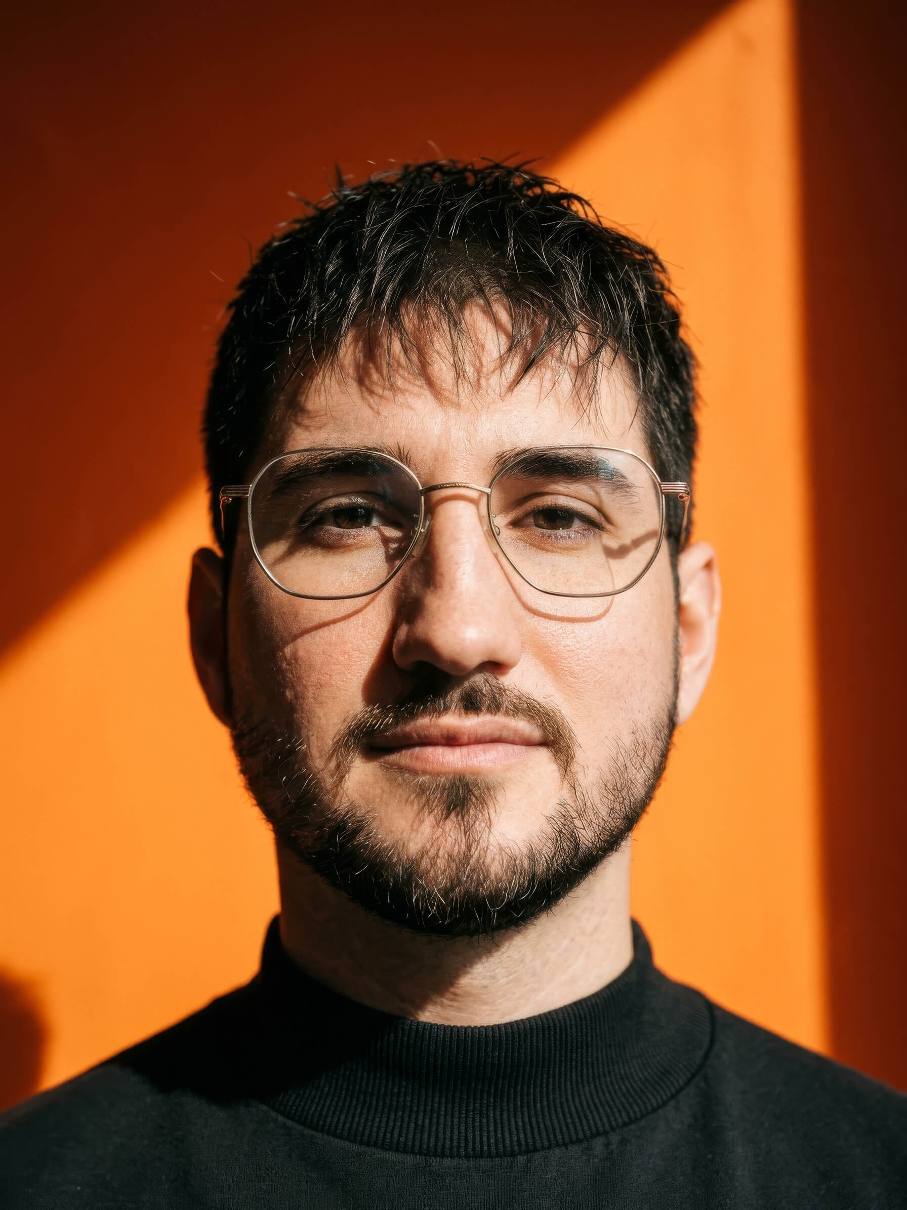Porträt von Timo Schüler vor orangefarbenem Hintergrund.